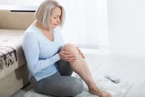 אישה יושבת כפופה בבית סובלת מכאבי ברך